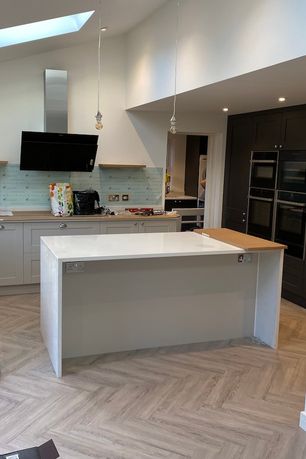 A white and grey kitchen renovation with a white island set ontop of a herringbone flooring