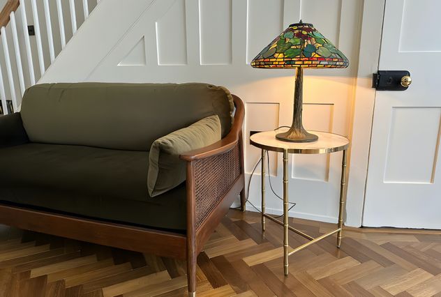 A traditional seating room with woodern herringbone flooring with a green 2 seater sofa and table lamp next to it