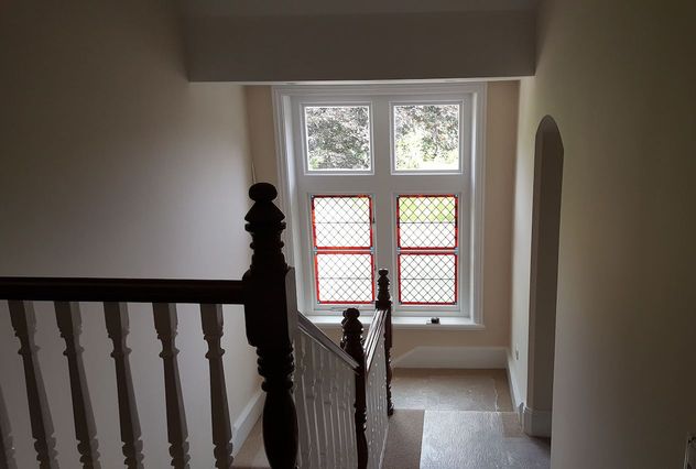 A look down the stairs to a landing area which has been fully decorated and the stained glass window repaired and the frame replaced with a white sash