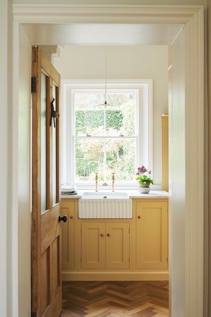 A kitchen with a belfast sink set below a sash window, yellow cabinets, and marble worktops